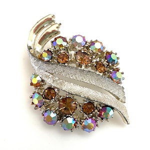 May include: A silver tone brooch with a swirl design and iridescent and brown rhinestones.