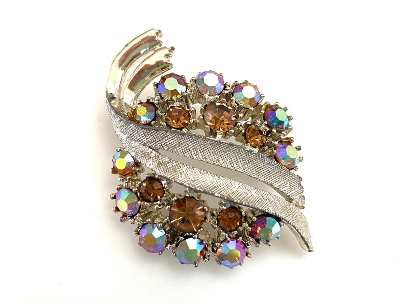 May include: A silver tone brooch with a swirl design and iridescent and brown rhinestones.