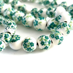 May include: A strand of white ceramic beads with a green floral pattern. The beads are round and have a smooth finish.