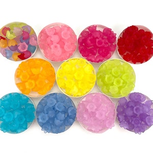 May include: Assortment of colorful flower-shaped resin beads in various shades of pink, red, orange, yellow, green, blue, and purple. The beads are arranged in small bowls on a white background.