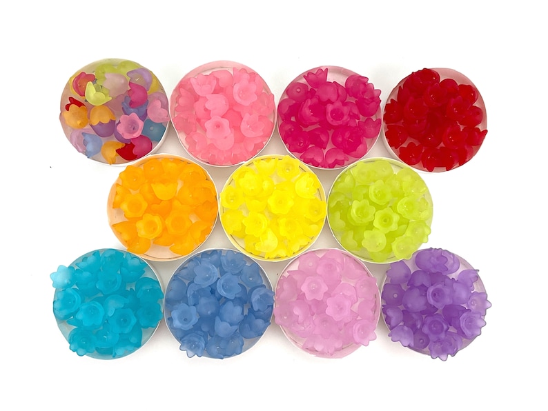 May include: Assortment of colorful flower-shaped resin beads in various shades of pink, red, orange, yellow, green, blue, and purple. The beads are arranged in small bowls on a white background.