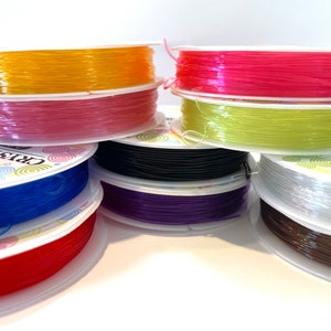May include: Assortment of colorful elastic string spools, including yellow, pink, green, black, purple, white, red, and brown. The spools are labeled "Crystal Stretch".