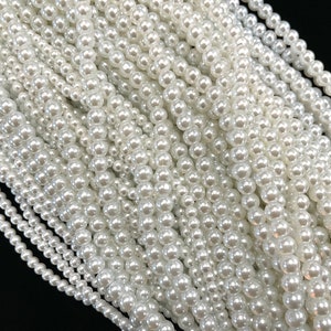 May include: A close-up of a strand of white pearl beads. The beads are round and smooth, and they are arranged in a tight, even pattern.