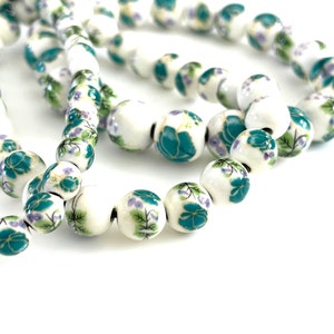 May include: A strand of white ceramic beads with a floral design. The beads are decorated with green and purple flowers.