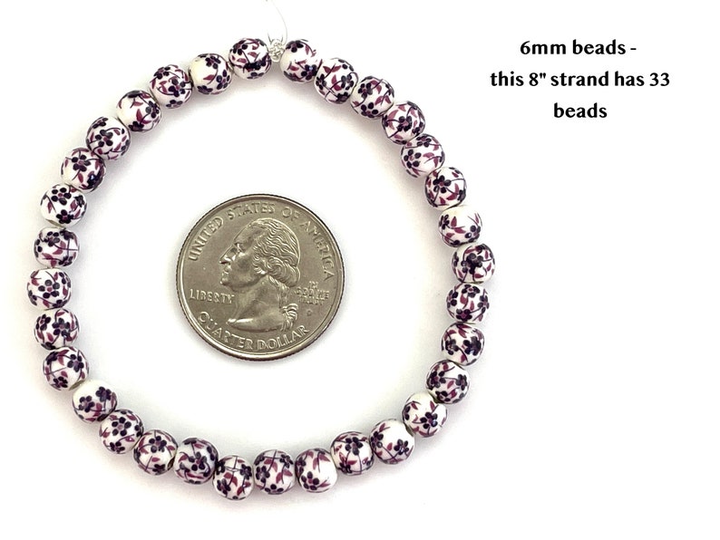 6mm porcelain ceramic beads with a purple floral pattern on a white background are strung in a loop that lies on a flat white background next to a quarter to show scale.