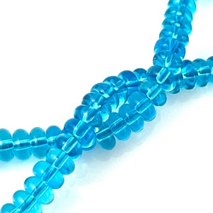 May include: A strand of light blue glass beads, each bead is round and has a faceted design.