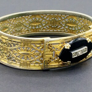 May include: A gold and silver filigree bracelet with a black onyx and diamond accent. The bracelet is intricately designed with a repeating pattern of geometric shapes.