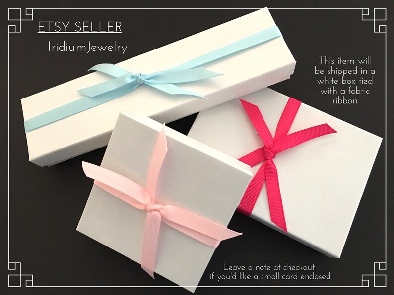 May include: Three white gift boxes with different colored ribbons. The boxes are tied with a light blue ribbon, a pink ribbon, and a hot pink ribbon. The text "This item will be shipped in a white box tied with a fabric ribbon" is printed on the right side of the image. The text "Leave a note at checkout if you'd like a small card enclosed" is printed on the bottom of the image.