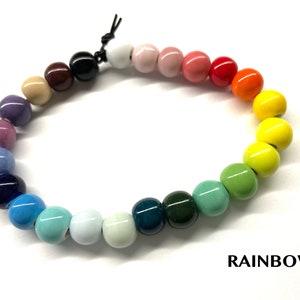 May include: A rainbow colored beaded bracelet with a black cord closure. The beads are arranged in a gradient from purple to green. The word "RAINBOW" is printed below the bracelet.