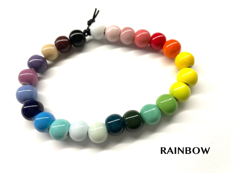 May include: A rainbow colored beaded bracelet with a black cord closure. The beads are arranged in a gradient from purple to green. The word "RAINBOW" is printed below the bracelet.