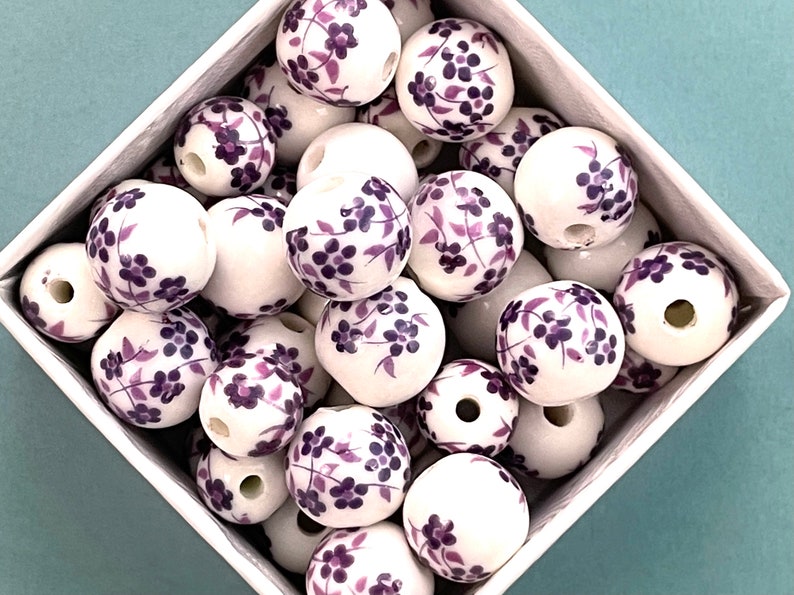 Loose round ceramic porcelain beads are piled loose within a diamond shape container that sits on a pale blue surface