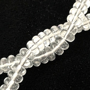 May include: A strand of clear quartz beads, strung together with a knotted thread. The beads are faceted and have a slightly irregular shape.