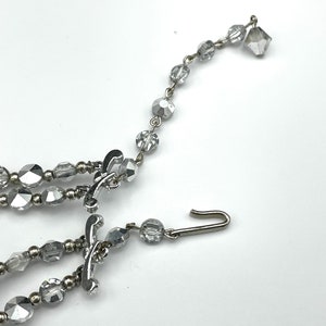 May include: A silver-toned necklace with multiple strands of faceted, clear beads. The necklace features decorative clasps and a hook closure. The beads are various shapes and sizes, reflecting light. The jewelry is set against a white background.