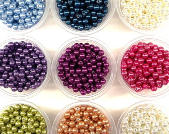May include: Nine clear plastic containers filled with round, smooth, glossy beads in various colors including light blue, dark blue, cream, purple, magenta, lime green, copper, and white, arranged in a three-by-three grid pattern.