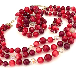 May include: A three-strand necklace, bracelet, and earrings set made of red and burgundy beads with clear crystal accents.