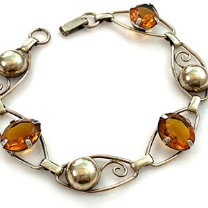 May include: A silver bracelet with a delicate design featuring amber-colored gemstones. The bracelet has a clasp closure and is made of a thin, wire-like material.
