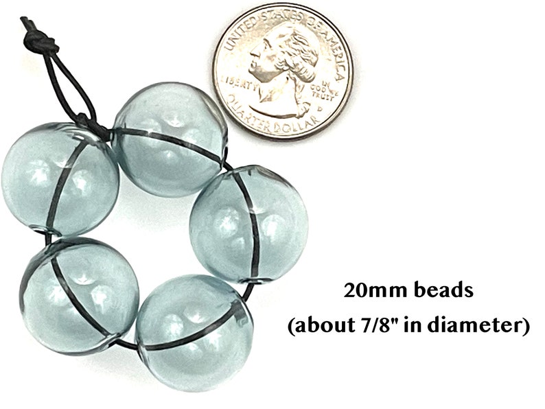 20mm hollow gray blue glass beads sit on a flat white surface next to a US quarter to show size.  These lampwork bubble beads have two holes and are grey with a light blue cast.