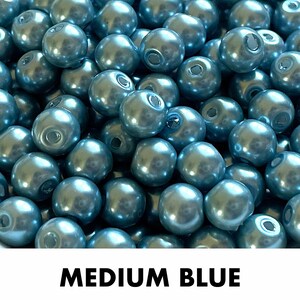 May include: A collection of round, medium blue beads with a smooth, lustrous finish. Each bead features a central hole for threading. The text "MEDIUM BLUE" is printed in bold black capital letters at the bottom of the image.