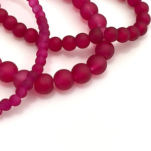 May include: A strand of pink frosted glass beads. The beads are round and have a matte finish.