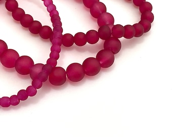 May include: A strand of pink frosted glass beads. The beads are round and have a matte finish.