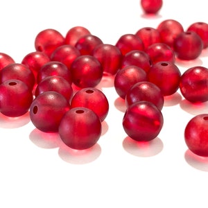 May include: A group of red, round, translucent beads scattered on a white surface. The beads are smooth and have a slight shine.