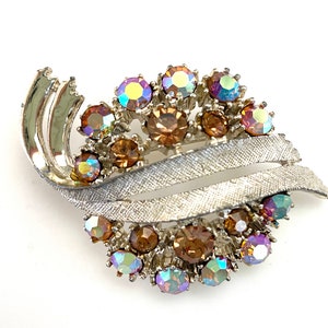 May include: A silver tone brooch with a swirl design and a cluster of iridescent and amber rhinestones.