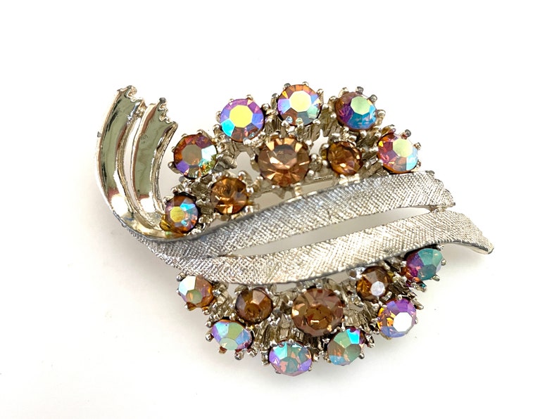 May include: A silver tone brooch with a swirl design and a cluster of iridescent and amber rhinestones.
