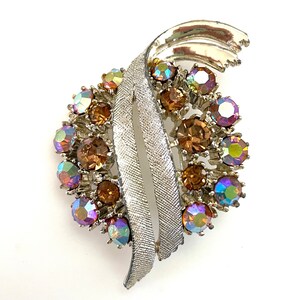 May include: A silver tone brooch with a swirl design and iridescent brown and purple rhinestones.