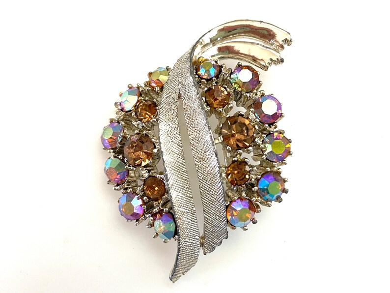 May include: A silver tone brooch with a swirl design and iridescent brown and purple rhinestones.