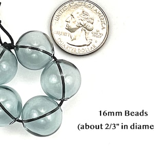16mm hollow gray blue glass beads sit on a flat white surface next to a US quarter to show size.  These lampwork bubble beads have two holes and are grey with a light blue cast.