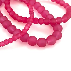 May include: Three pink frosted glass bead bracelets stacked on top of each other.