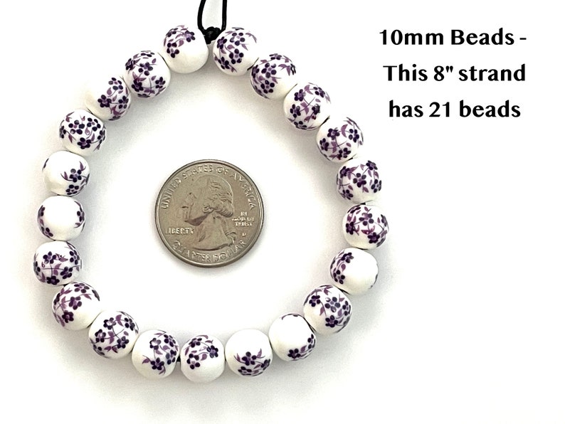 A circular strand of 10mm white porcelain ceramic beads with a purple floral print lie flat on a white surface next to a US quarter to show size.  Text in the upper right hand corner indicates that an 8 inch strand of 10mm beads includes 21 beads