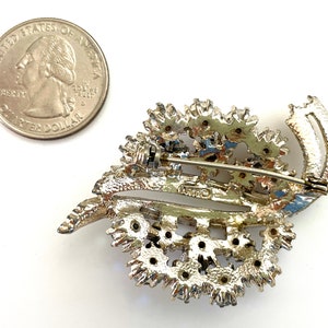 May include: Silver tone brooch with a leaf design and rhinestones. The brooch has a pin back and is marked "Coro".