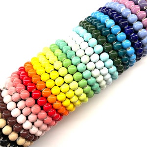 May include: A rainbow assortment of ceramic beads, stacked in a graduated pattern. The beads are round and glossy, with a variety of colors, including red, orange, yellow, green, blue, and purple.