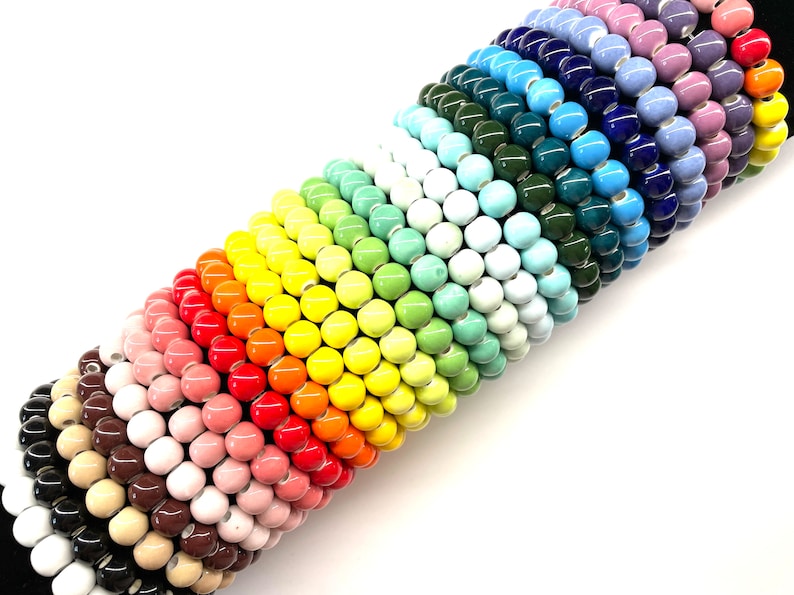 May include: A rainbow assortment of ceramic beads, stacked in a graduated pattern. The beads are round and glossy, with a variety of colors, including red, orange, yellow, green, blue, and purple.