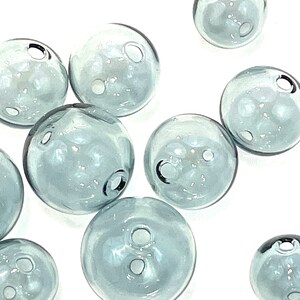 Top view of hollow gray blue glass beads sitting on a flat white surface.  These lampwork bubble beads have two holes and are shown in sizes  of 14mm 16mm and 20mm in diameter.  These are grey with a light blue cast.