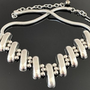 May include: A silver necklace with a geometric design. The necklace is made of a series of connected silver bars and beads.