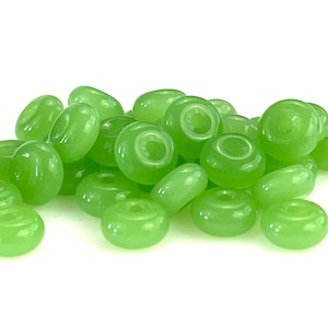 May include: A pile of light green glass beads with a donut shape. The beads have a smooth, glossy finish.