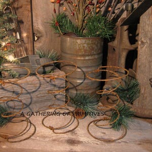 May include: Four rusty metal bed spring candle holders, arranged on a wooden surface. The candle holders are in various sizes and heights. A small potted plant with red berries is in the background.