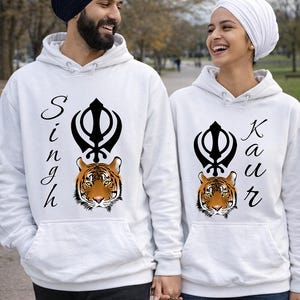 Peut inclure: Deux sweats à capuche blancs avec un motif de tigre et du texte. L'un dit "Singh" et l'autre "Kaur". Le tigre a des rayures orange et noires. Les sweats sont portés par deux personnes.