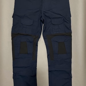 Puede incluir: Pantalones tácticos azul marino con múltiples bolsillos y paneles de rodilla reforzados. Los pantalones tienen un diseño de pierna recta y el texto "B.b.bridge" en la parte inferior.
