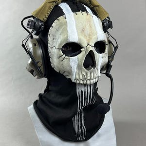 May include: A skull mask with a black hood and a tan head covering. The mask has white and tan stripes and stitched details. It features eye holes and a detailed skull design. A headset with a microphone is attached. The text "DarkSigth Panda" is at the bottom.
