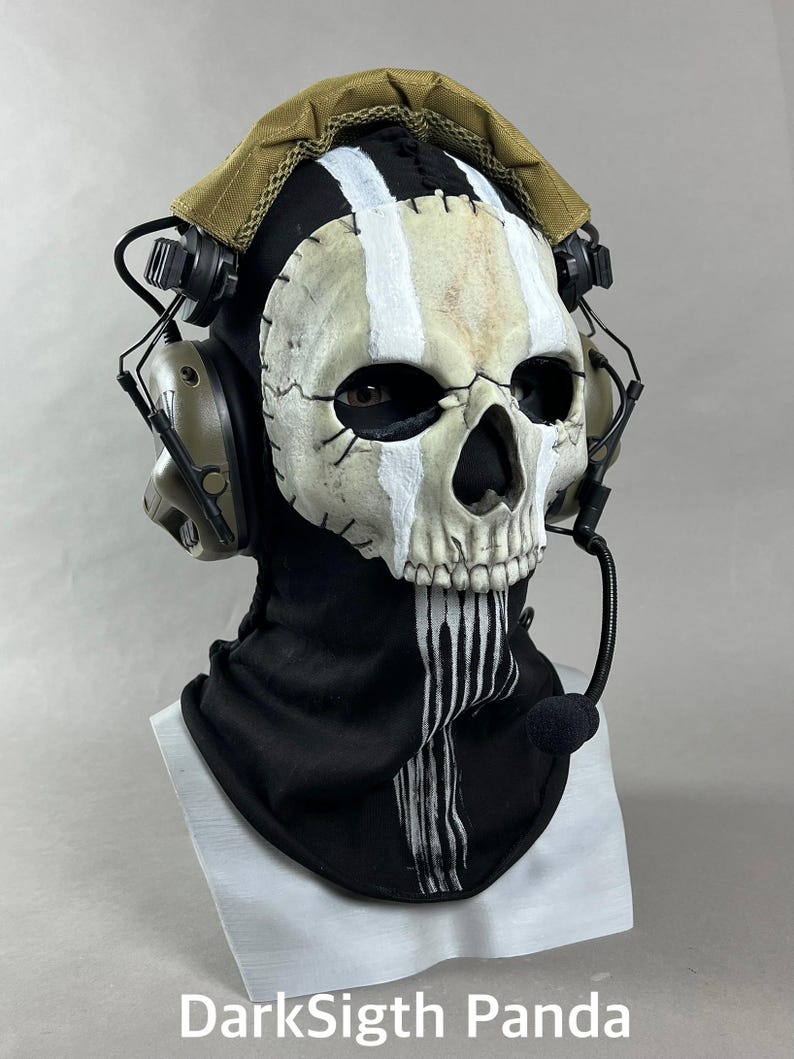 May include: A skull mask with a black hood and a tan head covering. The mask has white and tan stripes and stitched details. It features eye holes and a detailed skull design. A headset with a microphone is attached. The text "DarkSigth Panda" is at the bottom.