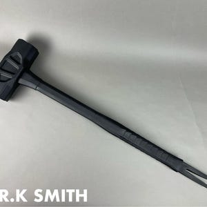 May include: A black multi-tool with a hammer head, a long handle, and a forked end. The tool has a textured grip on the handle. The text "A.R.K SMITH" is printed in white at the bottom of the image.