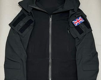 May include: Black tactical jacket with a hood, multiple pockets, and a zipper closure. Features a Union Jack patch on the upper arm and the text "A.R.K SMITH" at the bottom. The jacket has a modern, utilitarian design.