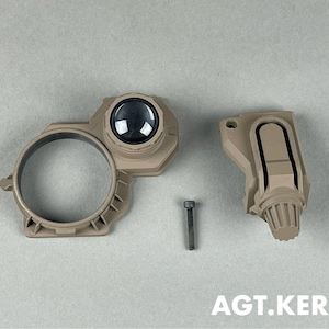 Puede incluir: Componentes de dispositivo táctico de color beige, que incluyen una pieza circular con una lente, una pieza rectangular y un tornillo. Los componentes están dispuestos sobre una superficie gris claro. El texto "AGT.KERRY" es visible en la parte inferior.