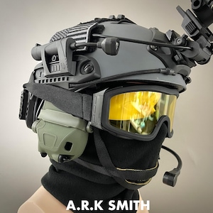 May include: A grey tactical helmet with attached goggles, headset, and a black balaclava. The goggles have yellow lenses. The helmet has a black and white striped patch. The text "A.R.K SMITH" is visible at the bottom.