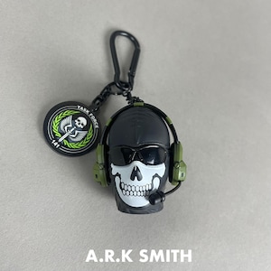 May include: A black and white skull-shaped keychain with sunglasses and a headset. The keychain has a black clasp and a circular tag with the text "TASK FORCE 141". The text "A.R.K SMITH" is at the bottom.