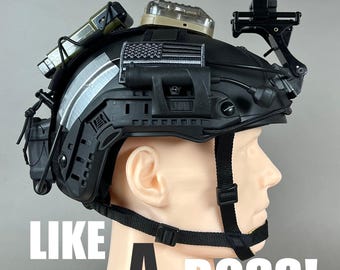 Pode incluir: Capacete tático preto com vários acessórios, incluindo luzes, suportes e um patch da bandeira americana. O capacete tem uma cinta de queixo e o texto "LIKE A BOSS!" em letras maiúsculas brancas.
