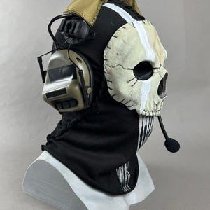 May include: A black and tan Ghost mask with a skull design, white vertical stripe, and attached headset. The mask is on a white stand. The text "DarkSigth Panda" is at the bottom.